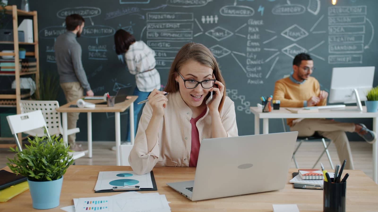 Woman celebrating a growth win on a business call at her laptop, surrounded by data charts